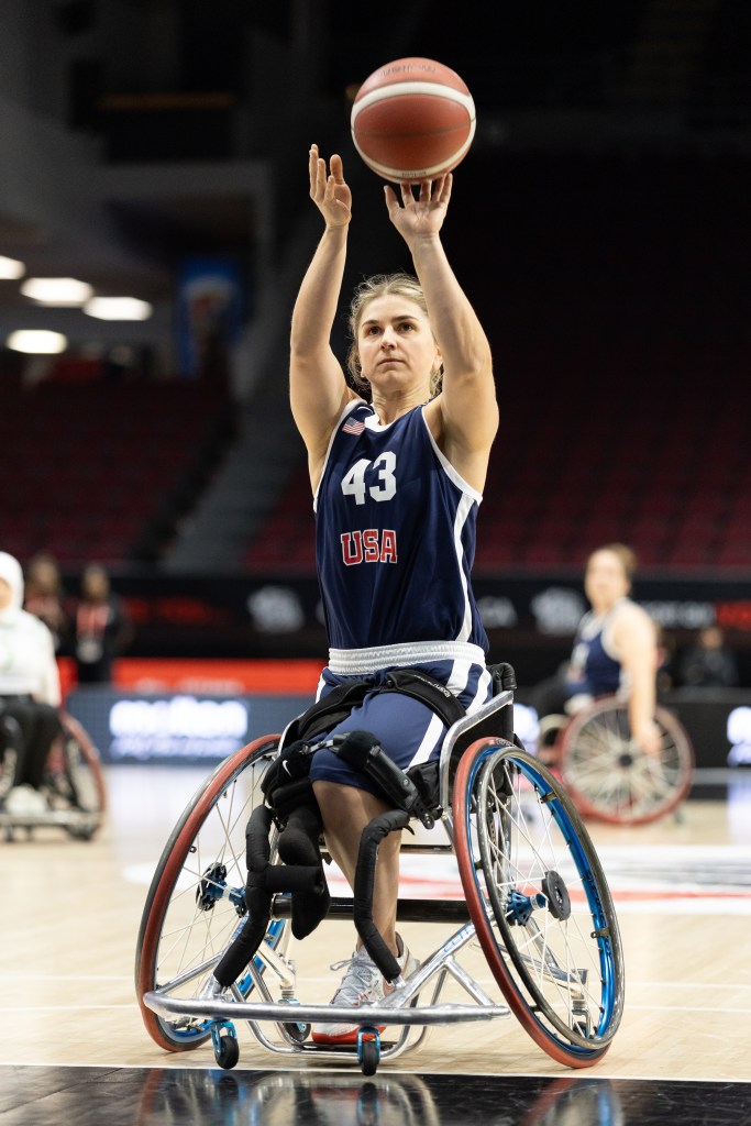 A female wheelchair basketball player from Team USA prepares to shoot a basketball during a game, wearing a navy jersey with the number 43.