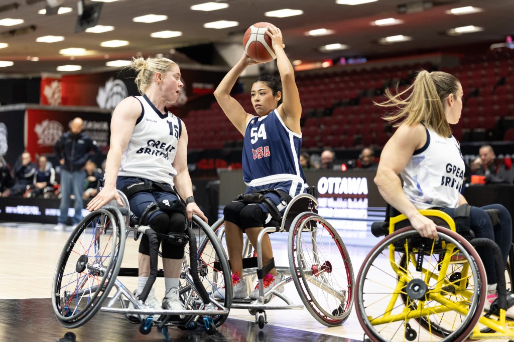 Two female wheelchair basketball players on a court, one from Team USA preparing to shoot the ball while the other from Great Britain defends.