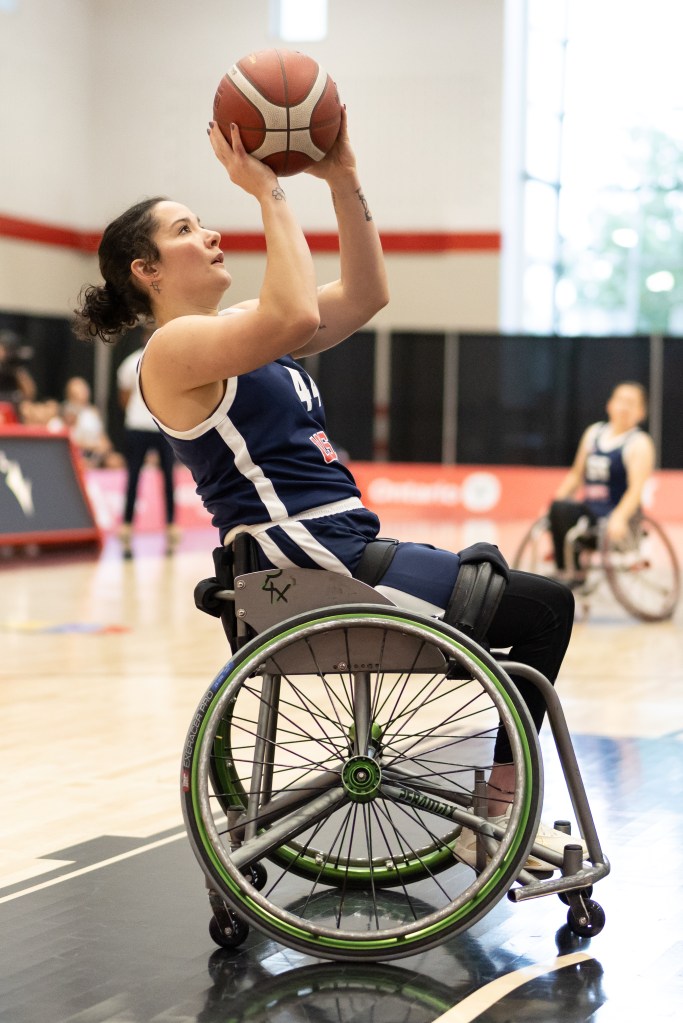 A female athlete in a wheelchair is preparing to shoot a basketball, showcasing determination and skill on the court.