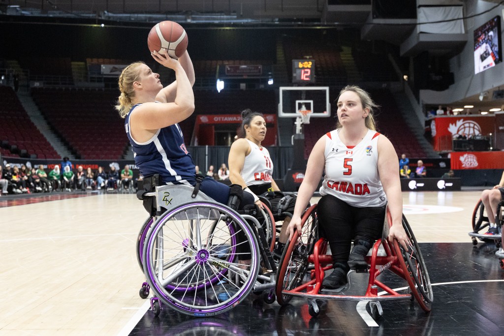A female wheelchair basketball player preparing to shoot while two other players watch during a game.